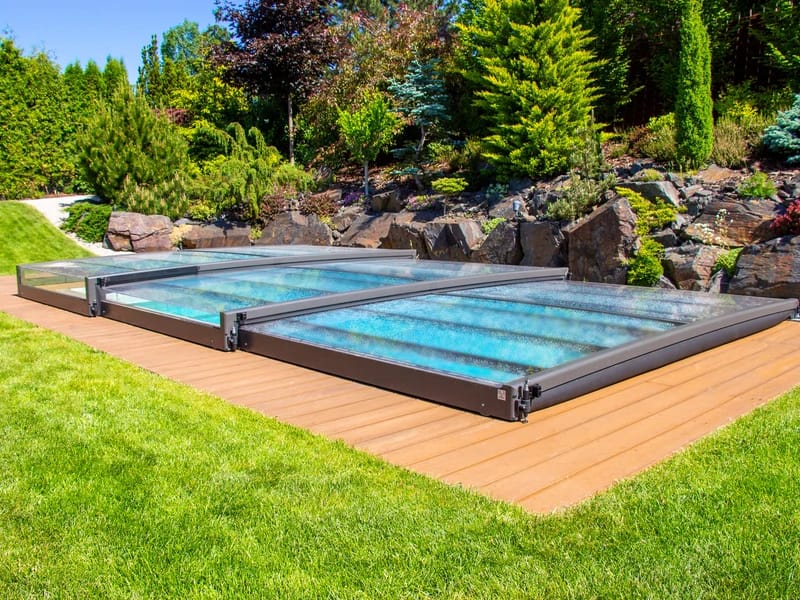 Niedrige, flache Poolüberdachung aus Aluminium und Glas komplett geschlossen über einem Pool auf einer Holzterrasse