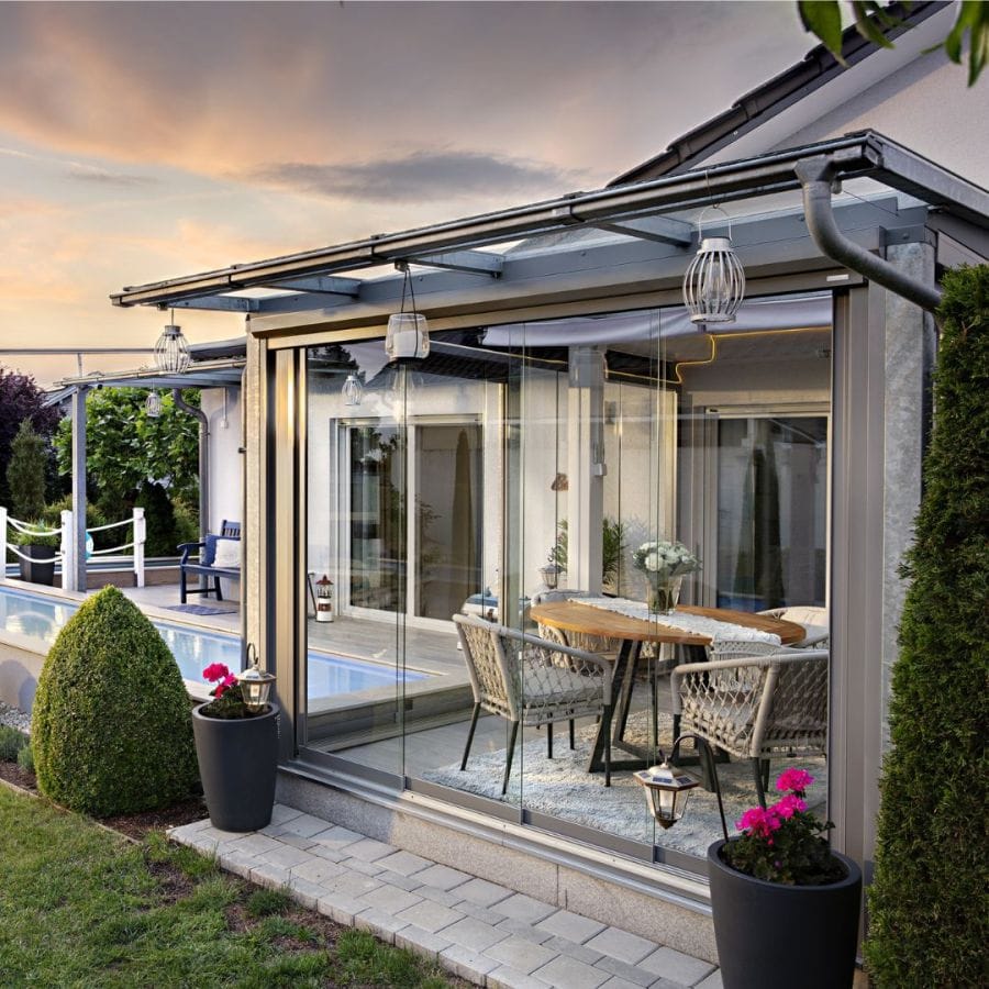 Geschlossene Terrassenüberdachung mit Glas-Schiebeelementen, Esstisch mit Rattanstühlen im Abendlicht