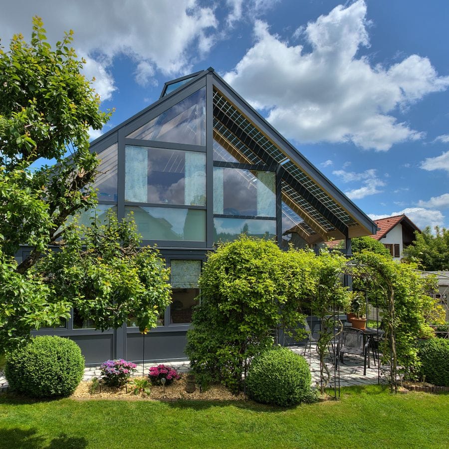 Mehrgeschossiger Glasanbau mit dunklem Dachglas und integrierter Solartechnik