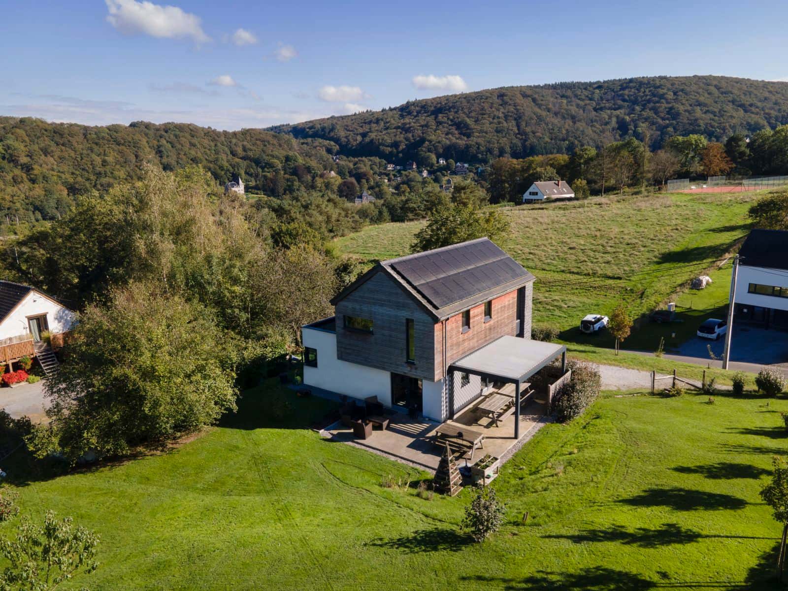 Luftaufnahme eines Wohnhauses mit kleiner freistehender Lamellendach-Terrassenüberdachung im Grünen
