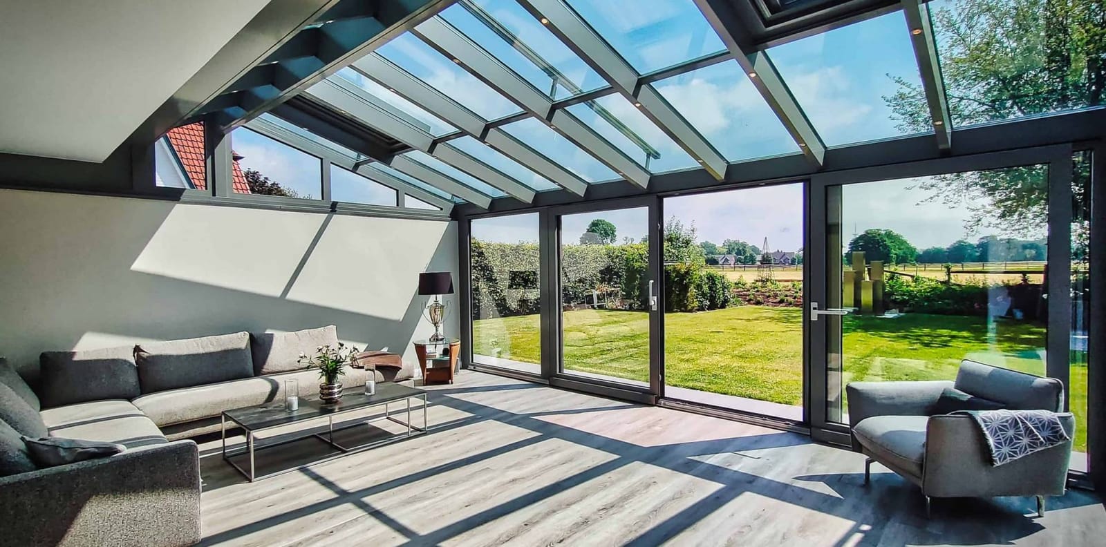 GEWE Aluminium-Wintergarten von innen mit Panoramaglasdach, Loungemöbeln und Blick in den Garten