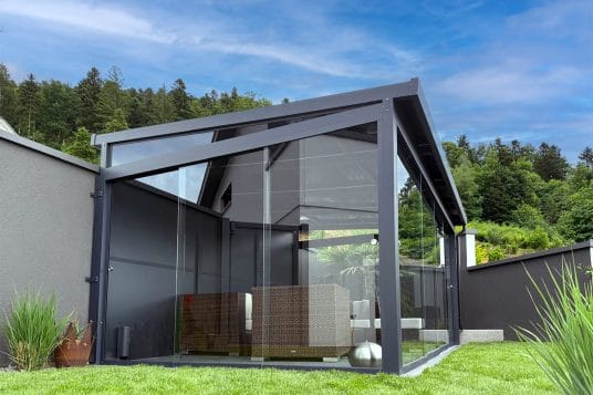 gutta Gartenzimmer aus anthrazitfarbenem Aluminium mit geschlossenen Glasschiebeelementen im Garten
