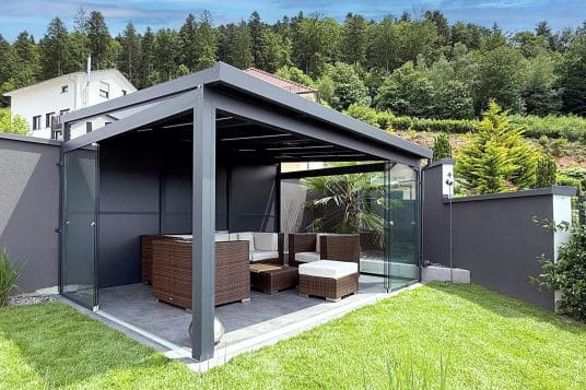 gutta Gartenzimmer mit geöffneten Glasschiebeelementen und Lounge-Möbeln im Sommer