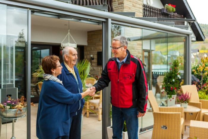 Kunde und Mitarbeiter eines Wintergartenbauers beim Handschlag vor dem fertigen Glashaus (Kalverkamp)