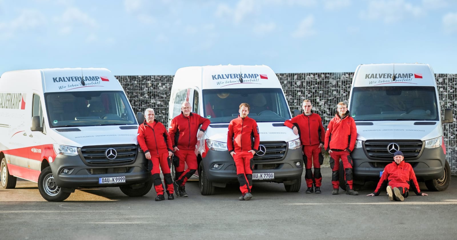 Montageteam in roter Arbeitskleidung vor drei Montagefahrzeugen eines Fachbetriebs (Kalverkamp)