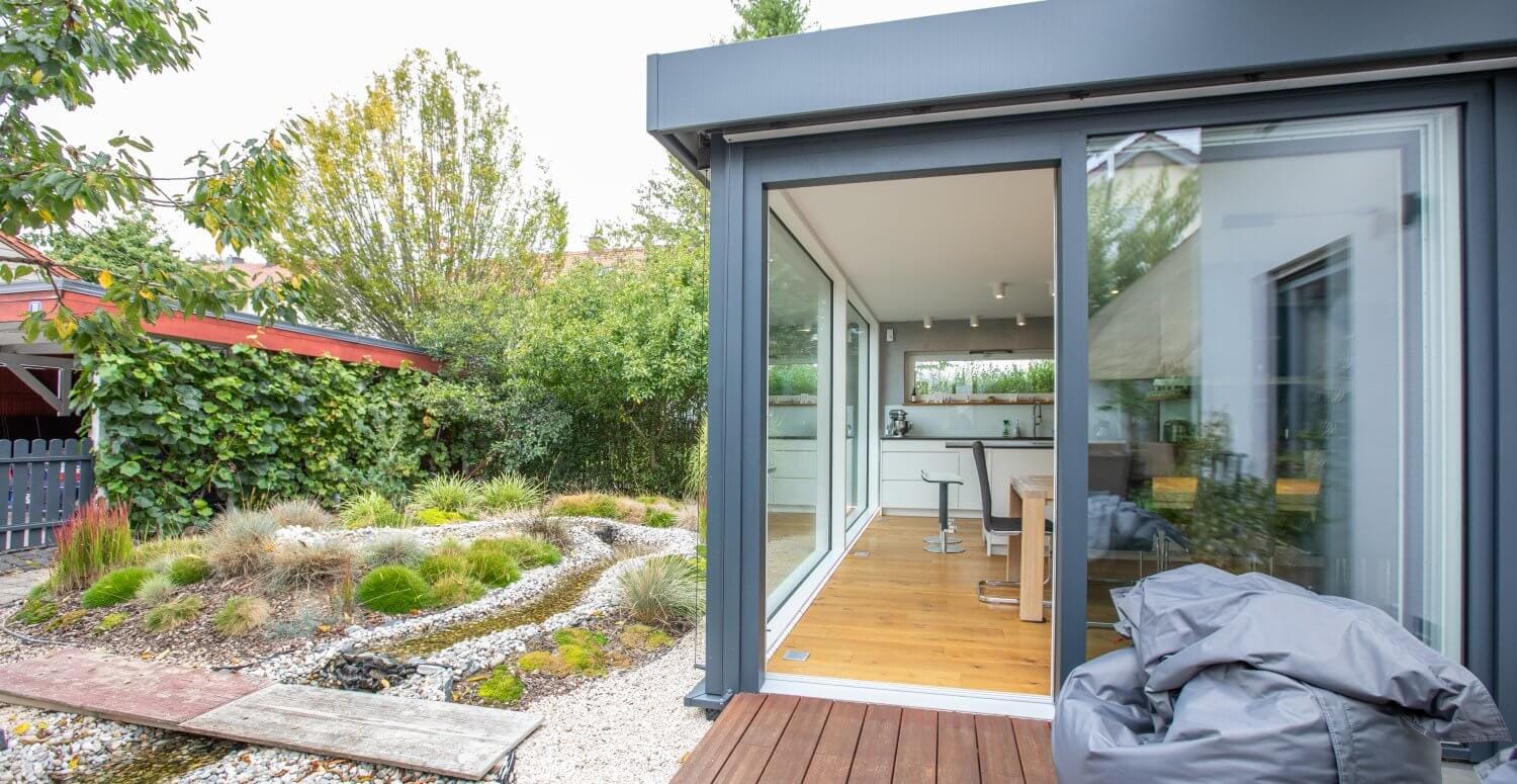 Kubisches, verglastes Gartenhaus mit klarer geometrischer Form, umgeben von Bäumen