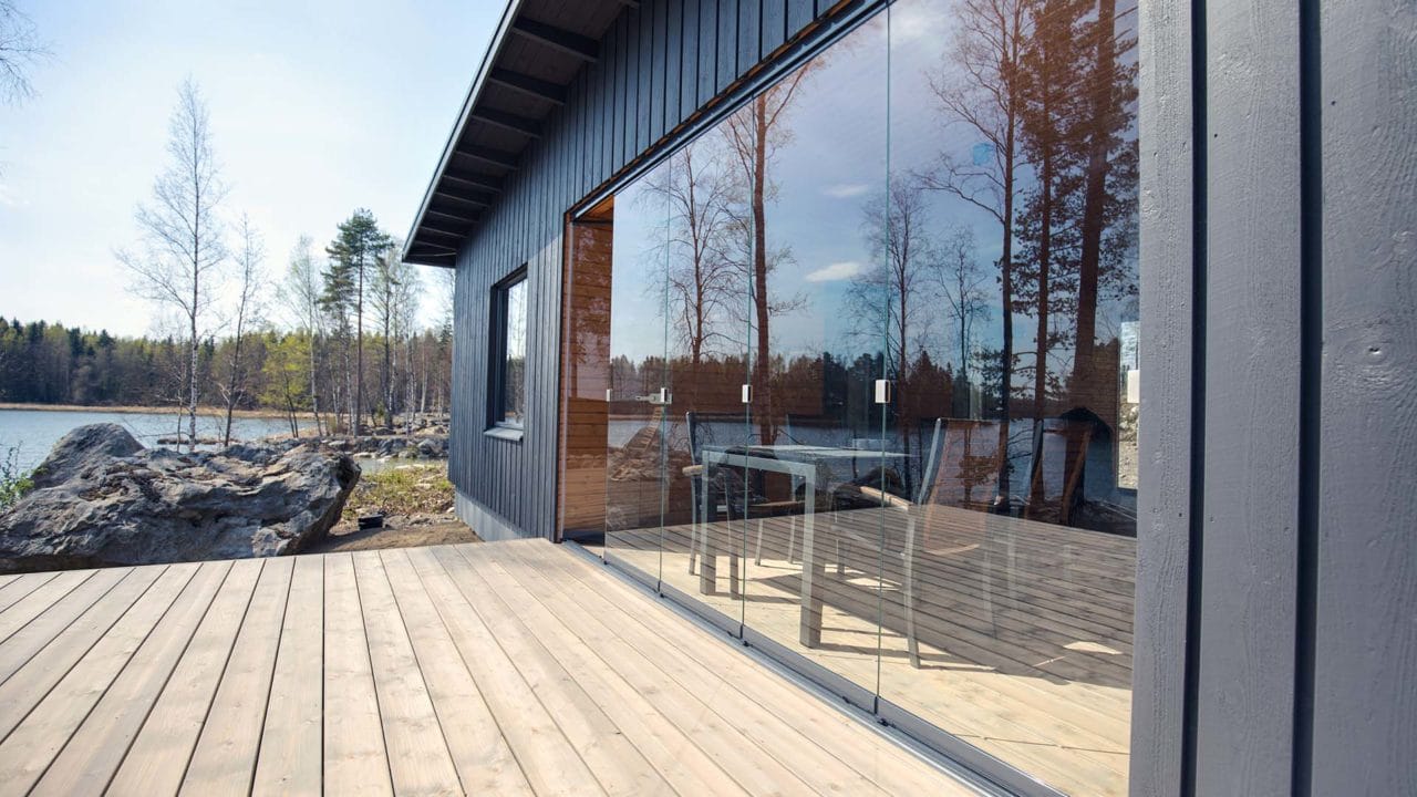 Rahmenlose Glas-Schiebeverglasung an einer Holzterrasse eines dunklen Holzhauses am See