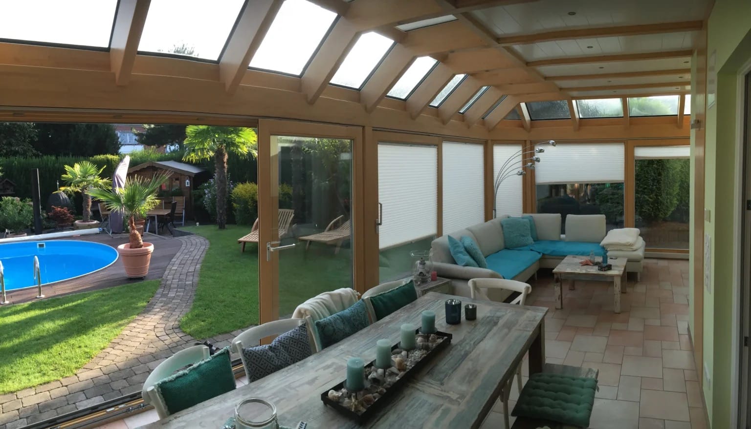 Holz-Aluminium-Wintergarten mit Holzsparren, Dachfenstern und Loungemöbeln, Blick auf Garten mit Pool