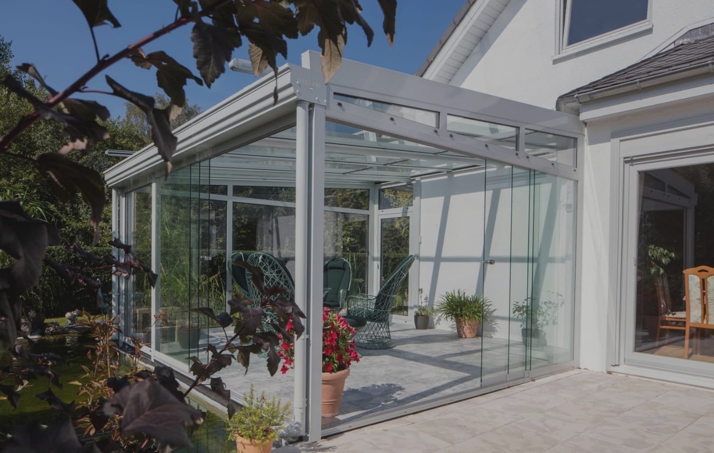 Kaltwintergarten aus Aluminium mit schiebbaren Glaselementen an einem weißen Haus, Terrasse mit Pflanzen