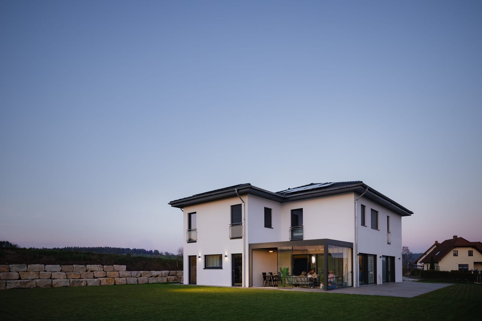 Pergolux-Pergola mit Glaswänden an einem Einfamilienhaus in der Abenddämmerung, innen beleuchtet