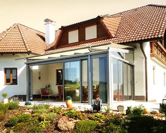 Wintergarten mit Aluminiumprofilen und Schiebeelementen an einem ländlichen Wohnhaus mit Ziegeldach