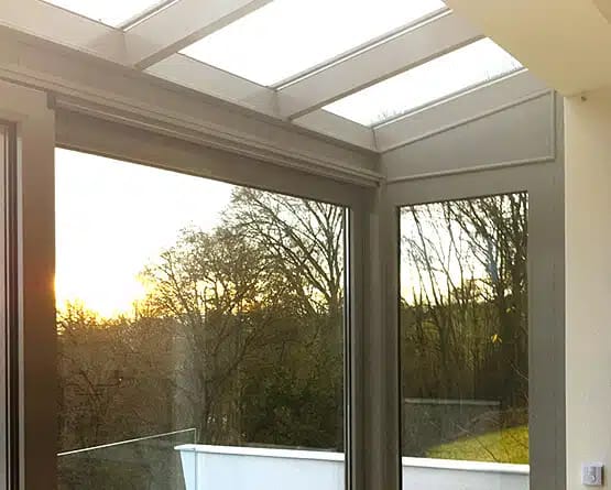 Glasdach-Innenansicht eines Wintergartens mit Blick auf Sonnenuntergang und Bäume