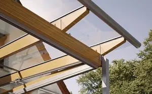 Holzsparren eines Terrassendachs mit Glaseindeckung von unten, Aluminium-Regenrinne und Baumkronen