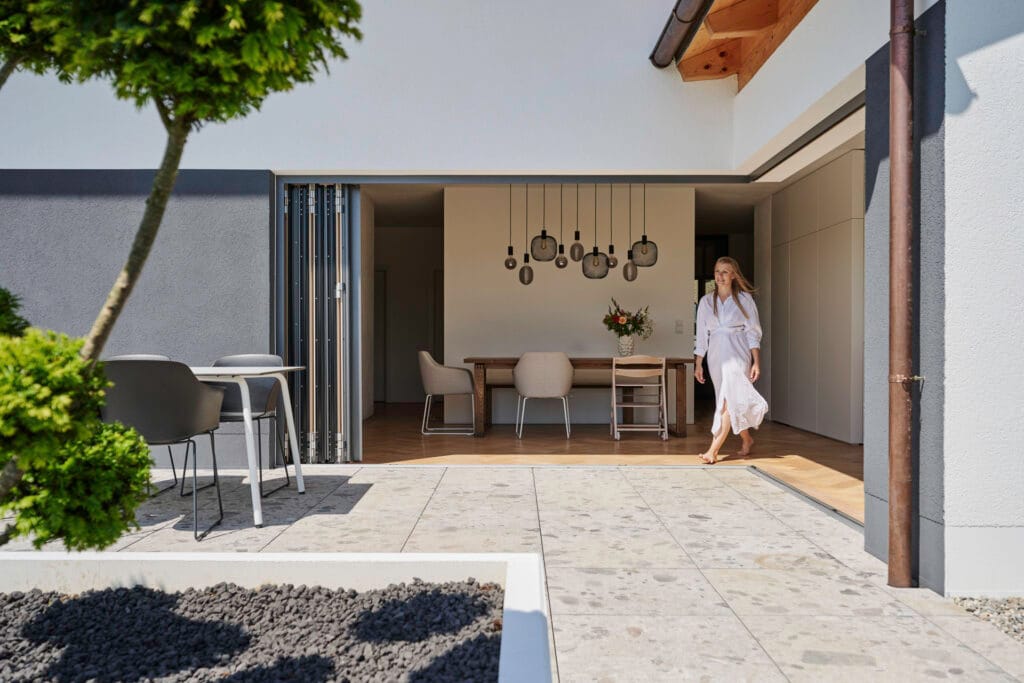 Solarlux Glas-Faltwand komplett geöffnet, Frau geht von Terrasse in Esszimmer mit Pendelleuchten