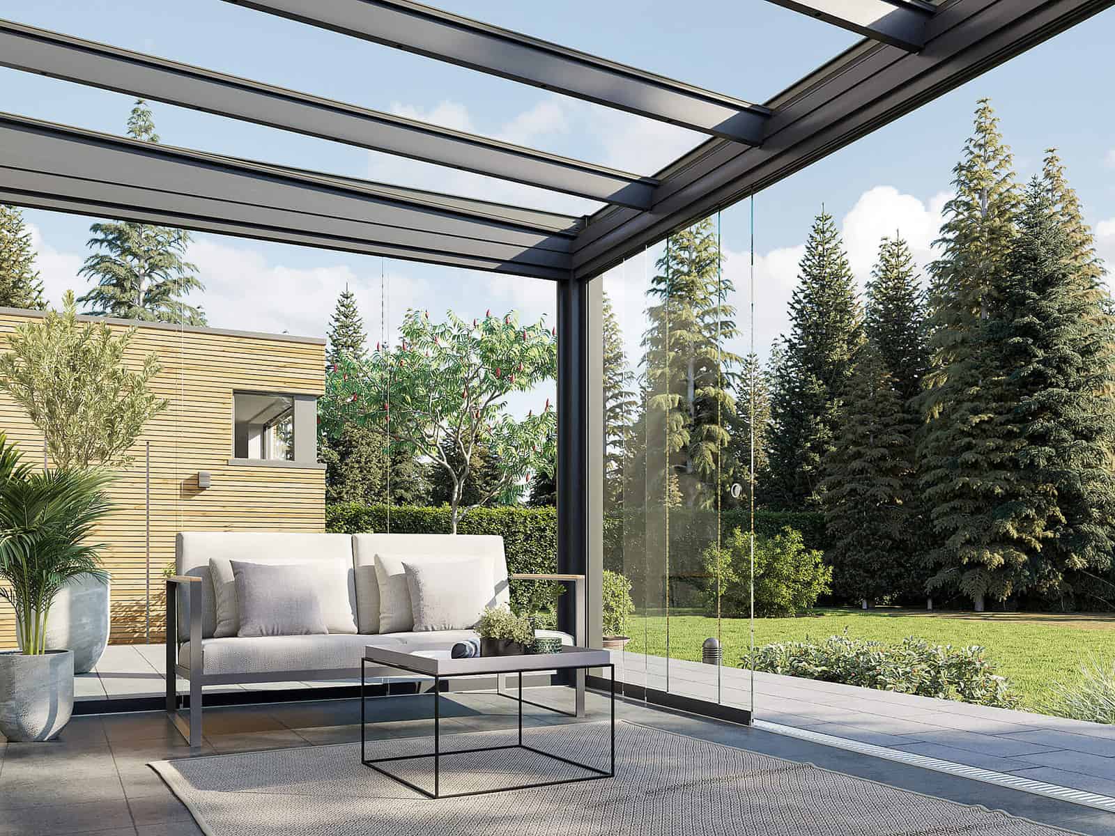 Filigrane Aluminium-Terrassenüberdachung mit Glasdach und Glas-Seitenwand, Lounge-Sitzgruppe, Nadelbäume im Hintergrund