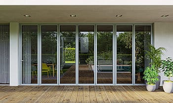 Geschlossene Glas-Faltwand aus schmalen Aluminiumflügeln an einer Terrasse mit Holzdielen, Blick in einen Garten