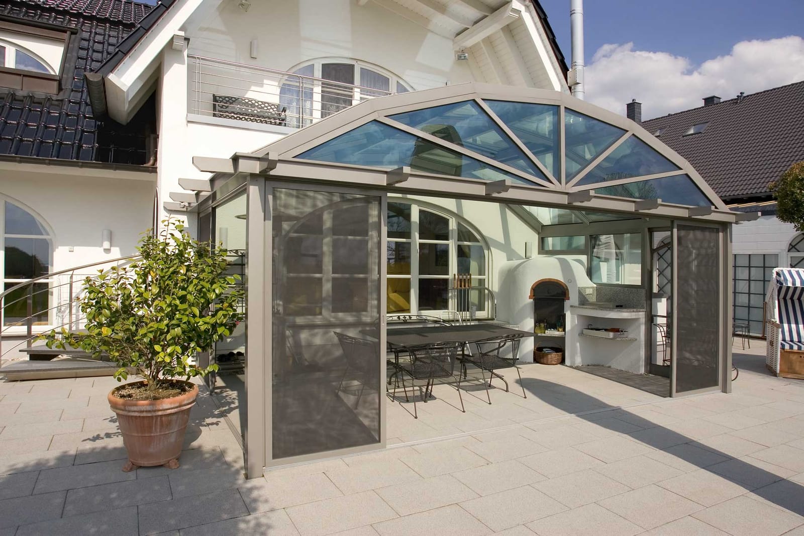 Sunshine Terrassenüberdachung mit gebogenem Glasdach, Außenküche und Sitzbereich