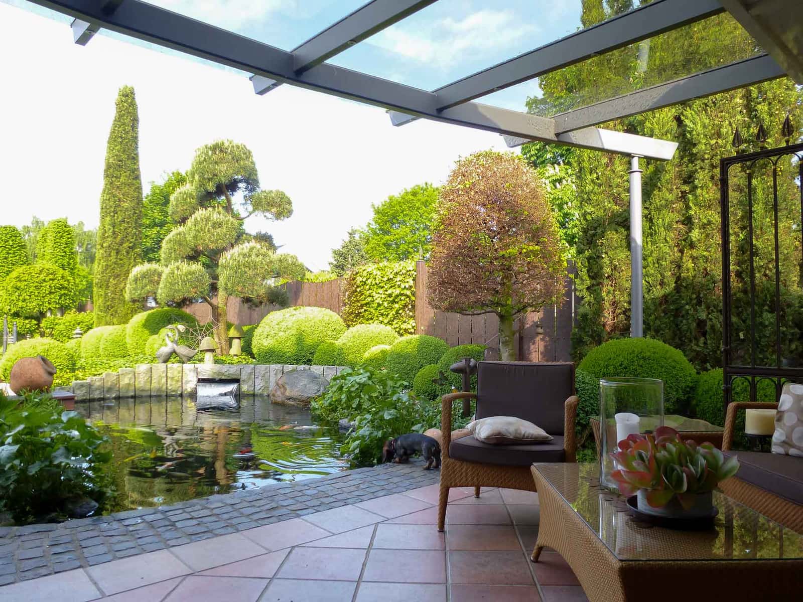 Sunshine Terrassenüberdachung an einem modernen Flachdachhaus mit Blick auf Gartenteich