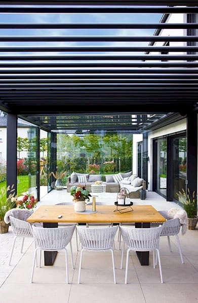 Terrasse mit Lamellendach über einer Sitz- und Essgruppe, Lamellen teilweise geöffnet (TS-Aluminium)